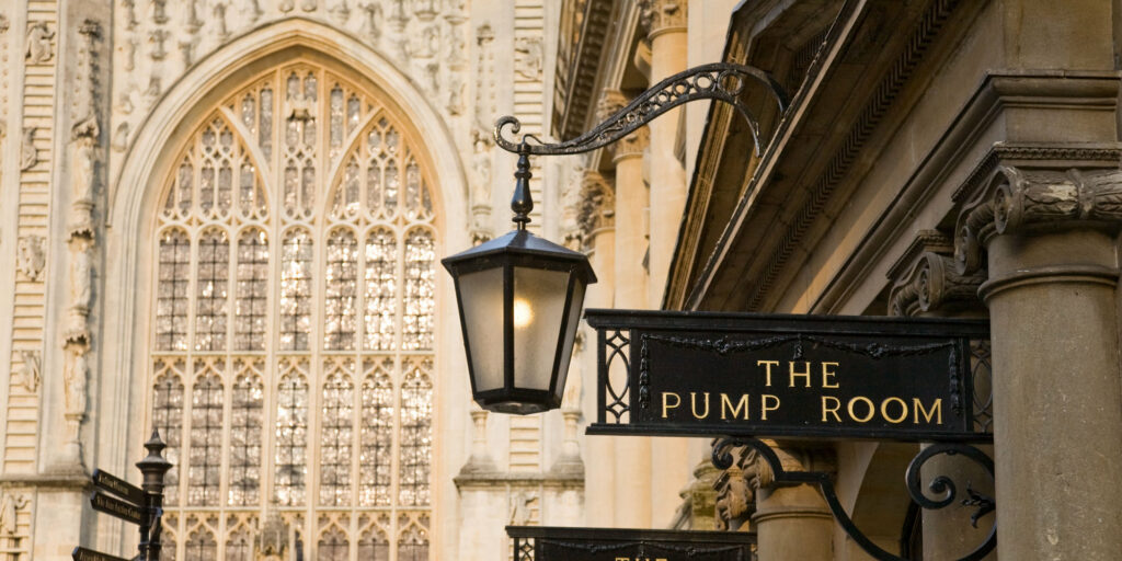 Bath Pump rooms exterior signs and columns with the west window of Bath Abbey in the background.